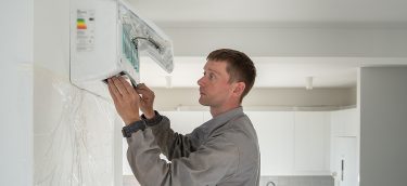 Man Professional Technician Worker Electrician In Uniform Instal Man professional technician worker electrician in uniform installing air conditioner in modern apartment on wall on kitchen. Maintenance and repair service concept. Climate control, split system.