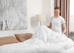 Young woman making bed in room. Space for text
