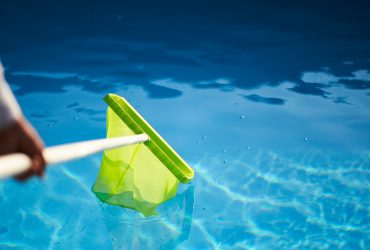 Man with skimmer net equipment cleaning swimming pool from rubbish. Service and maintenance of the pool. Male removes garbage from the water with a sap. Swimming pool cleaning service. Hotel cleaner.
