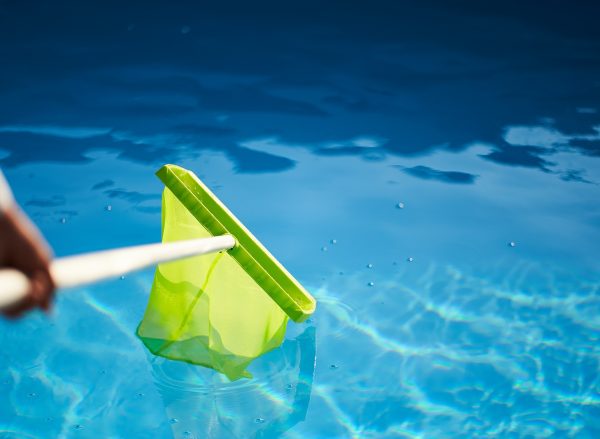 Man with skimmer net equipment cleaning swimming pool from rubbish. Service and maintenance of the pool. Male removes garbage from the water with a sap. Swimming pool cleaning service. Hotel cleaner.