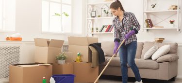 New Home Cleaning. Young Woman Tiding Up After Moving To New App New home cleaning. Young woman tiding up after moving to new appartment. Girl with various detergents, rags and mops in living room full of carton boxes. Household and spring-cleanig concept